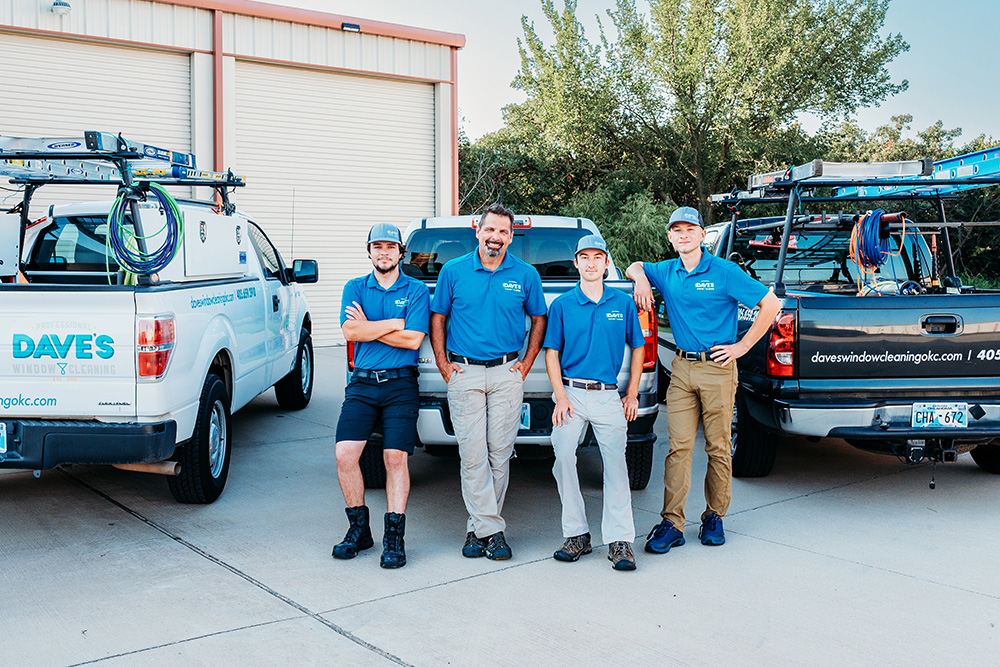Oklahoma City branding photos of four men in blue shirts stand confidently in front of two branded Dave's window cleaning trucks, conveying teamwork and professionalism.
