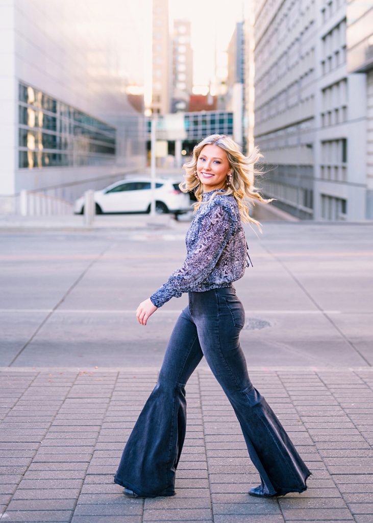 High school senior girl walking in downtown Oklahoma City wearing coordinated outfit during urban senior portrait session