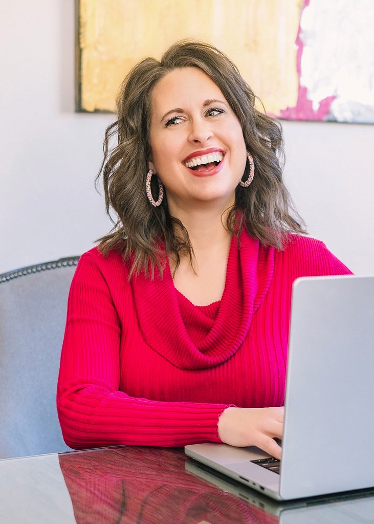 a smiling person sitting at a desk with a laptop