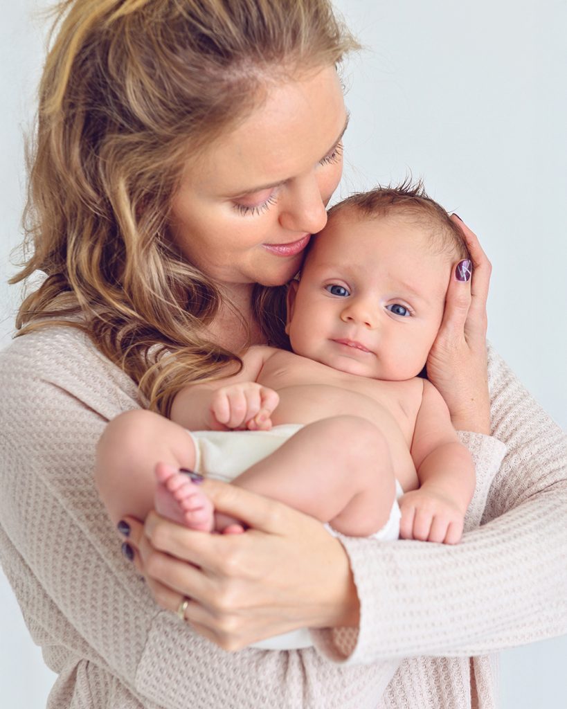 A woman lovingly cradles a baby in her arms, gently touching her cheek to the baby's head.