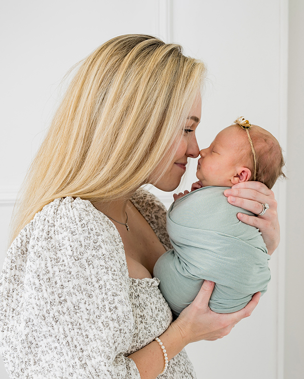 A woman gently holds a sleeping newborn wrapped in a soft green blanket, their noses touching at Rose + Salt Studio in Edmond, OK.