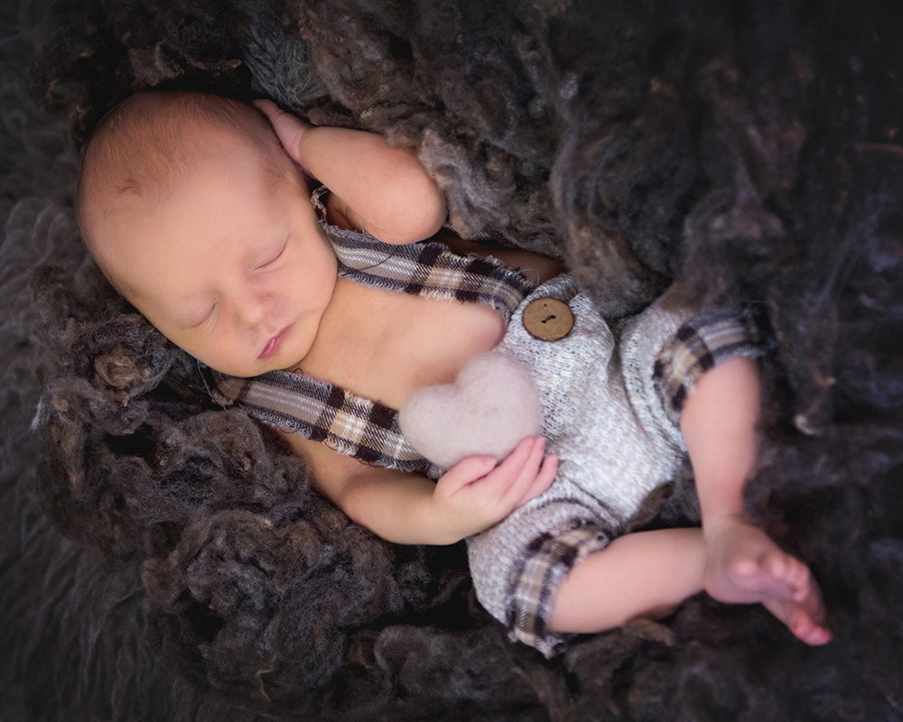 Newborn baby peacefully sleeping, wrapped in a soft, pink blanket, surrounded by textured fur on a pastel backdrop.