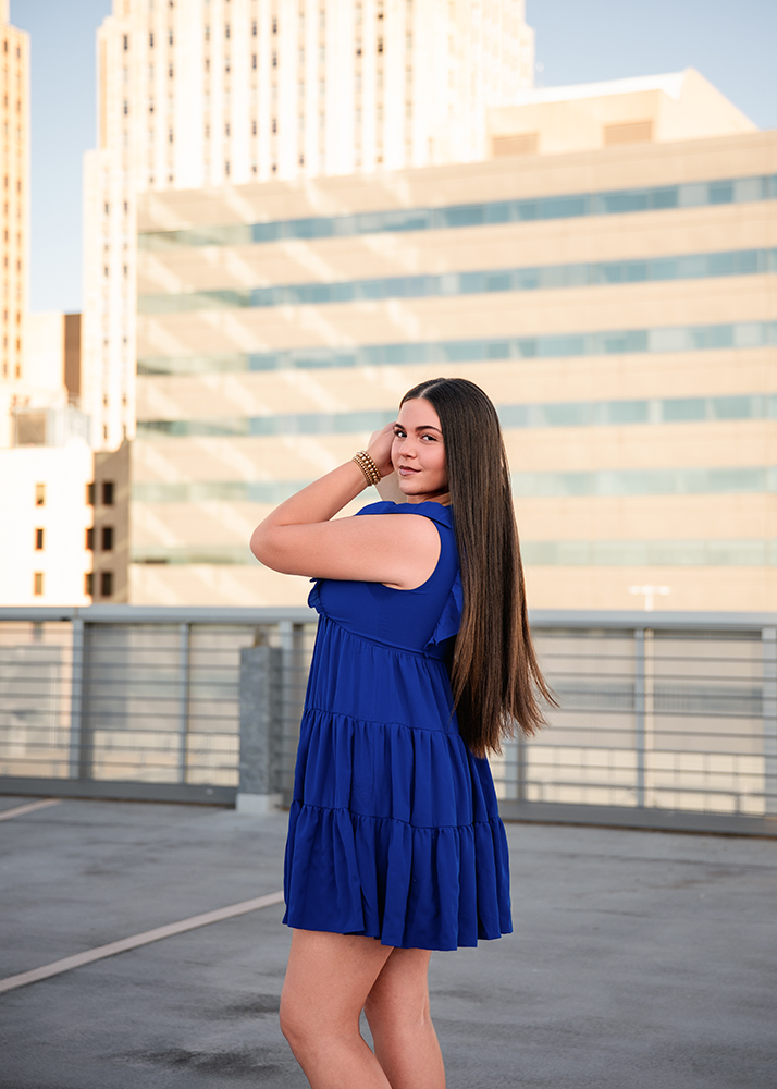 Peyton poses confidently on a rooftop with the Oklahoma City skyline for her senior photos. Her long hair flows down her back, and she wears a thoughtful expression.