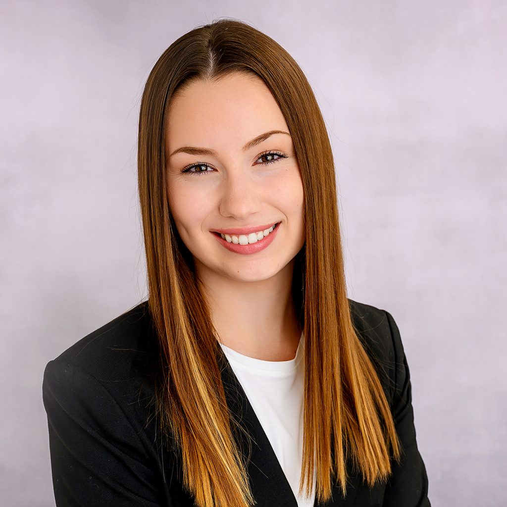 Oklahoma headshot of young woman with long straight hair smiles warmly against a soft gray background