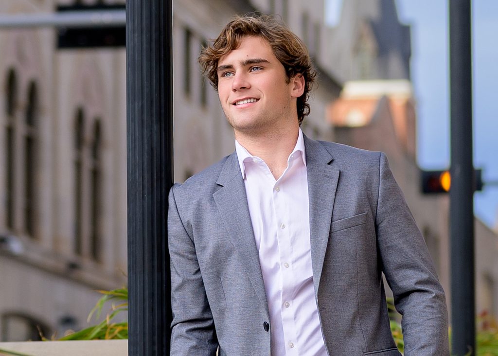 High school senior boy in suit posing outdoors in urban Oklahoma City during senior portrait session