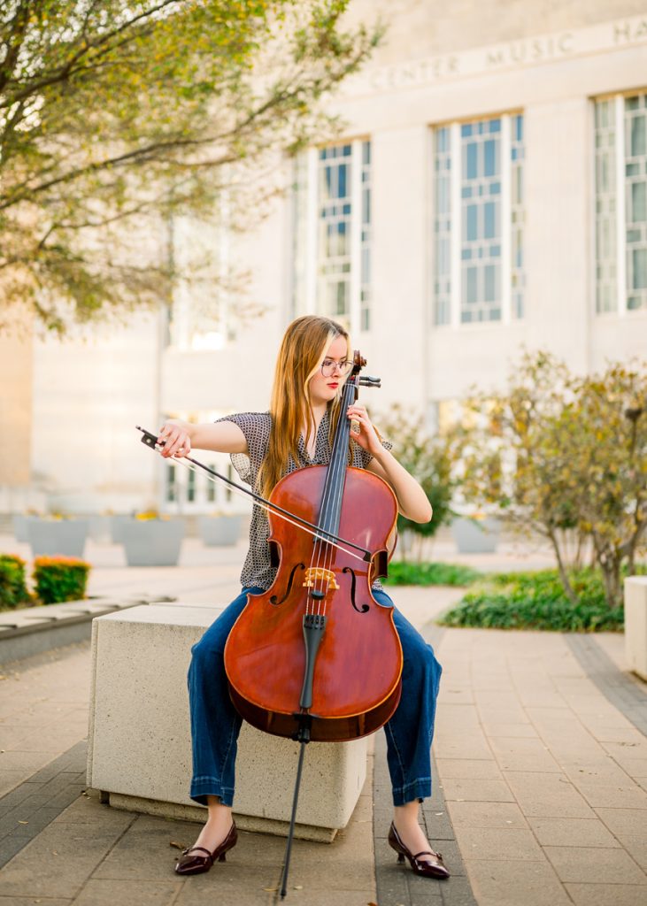 High school senior girl playing cello outdoors in Oklahoma City during senior portrait session with musical instrument