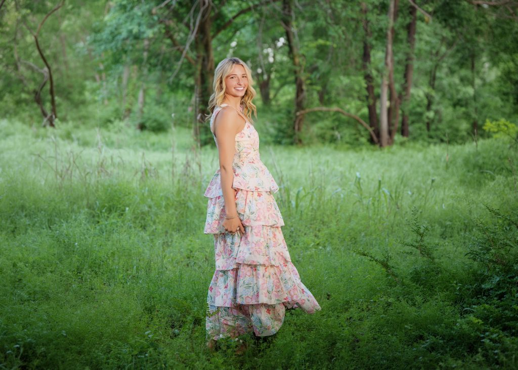 High school senior girl in floral dress standing in green field during Oklahoma City outdoor senior portrait session