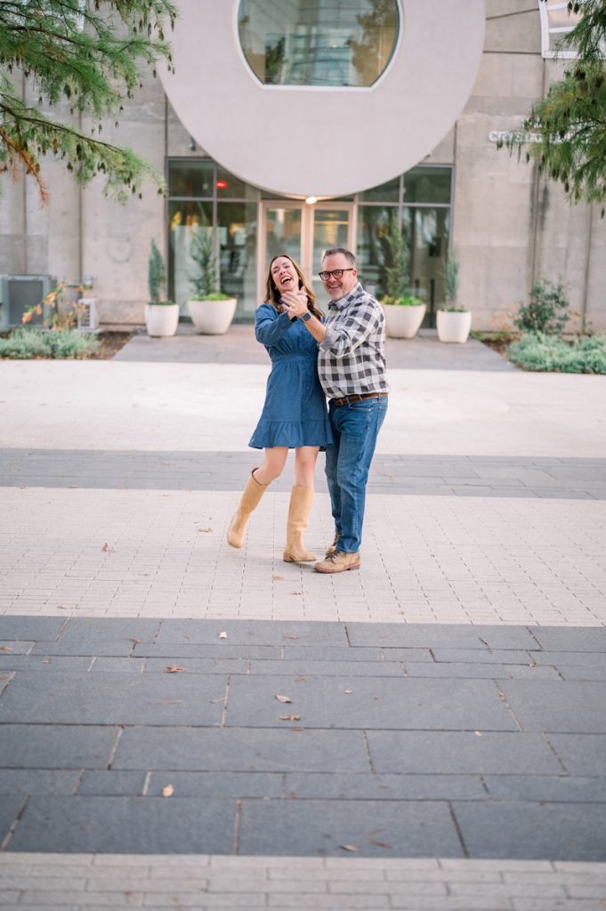 Couple dancing together outside a modern downtown Edmond building during a fun portrait session in Oklahoma.