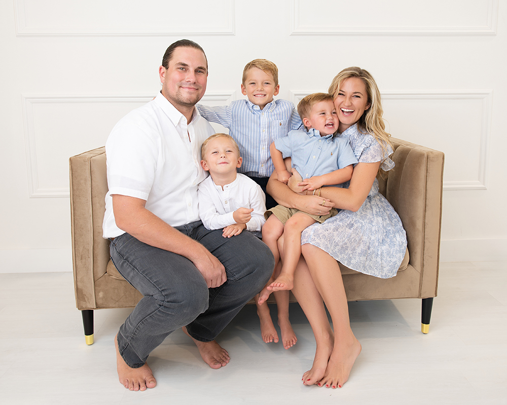 Young family with three boys sitting together on a couch during a studio family portrait session in Edmond, Oklahoma.