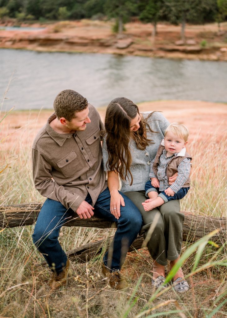 Young family sitting together on a log near the water during a fall family photography session in Edmond, Oklahoma.
