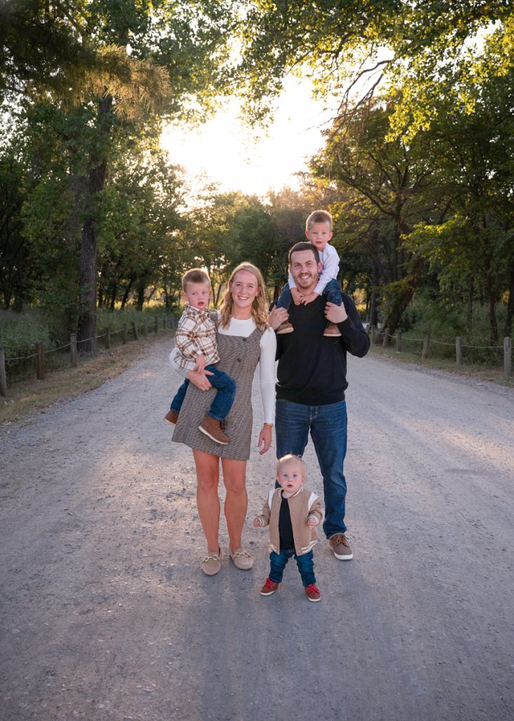 Family of five posing together on a tree-lined road during a fall family photography session in Edmond, Oklahoma.