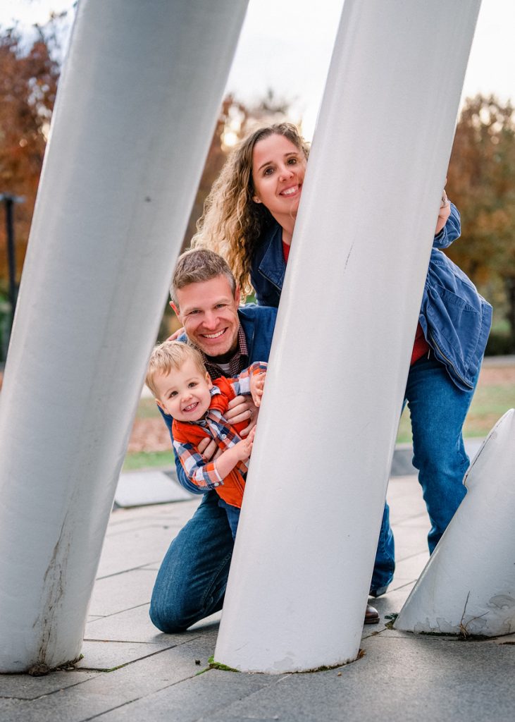 Parents and toddler smiling and playing around a modern sculpture during a family photography session in Oklahoma City.